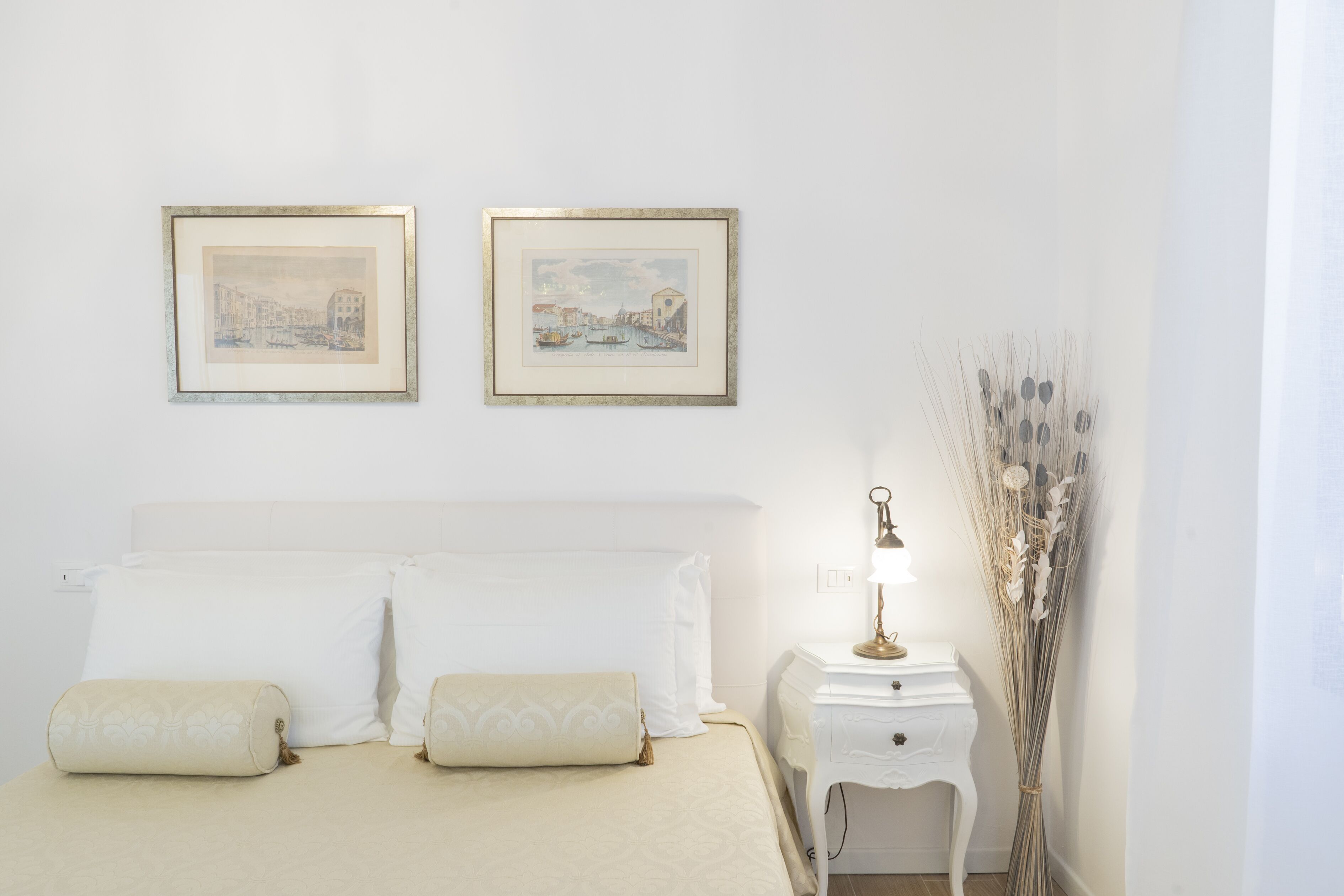 Une chambre à coucher bien rangée, avec un lit, deux tableaux encadrés au mur, une table de chevet avec une lampe et un vase décoratif.