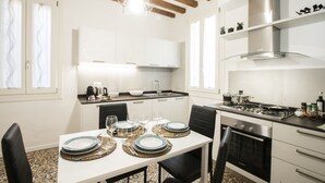 A modern kitchen with white cabinets, a stainless steel stove, and a dining area set for four with plates and glasses. - Giò&Giò Apartments (Venice)
