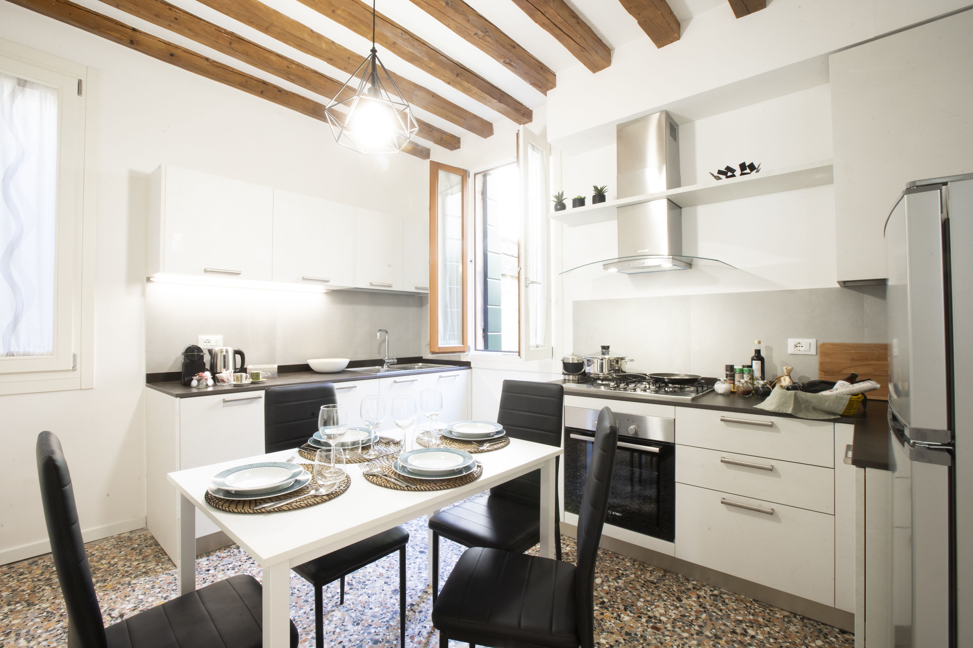 Une cuisine moderne avec des meubles blancs, une table à manger pour quatre personnes et un poêle noir.
