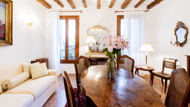 A dining room with a wooden table, chairs, a vase with flowers, a chandelier, and a painting on the wall. - Giò&Giò Apartments (Venice)