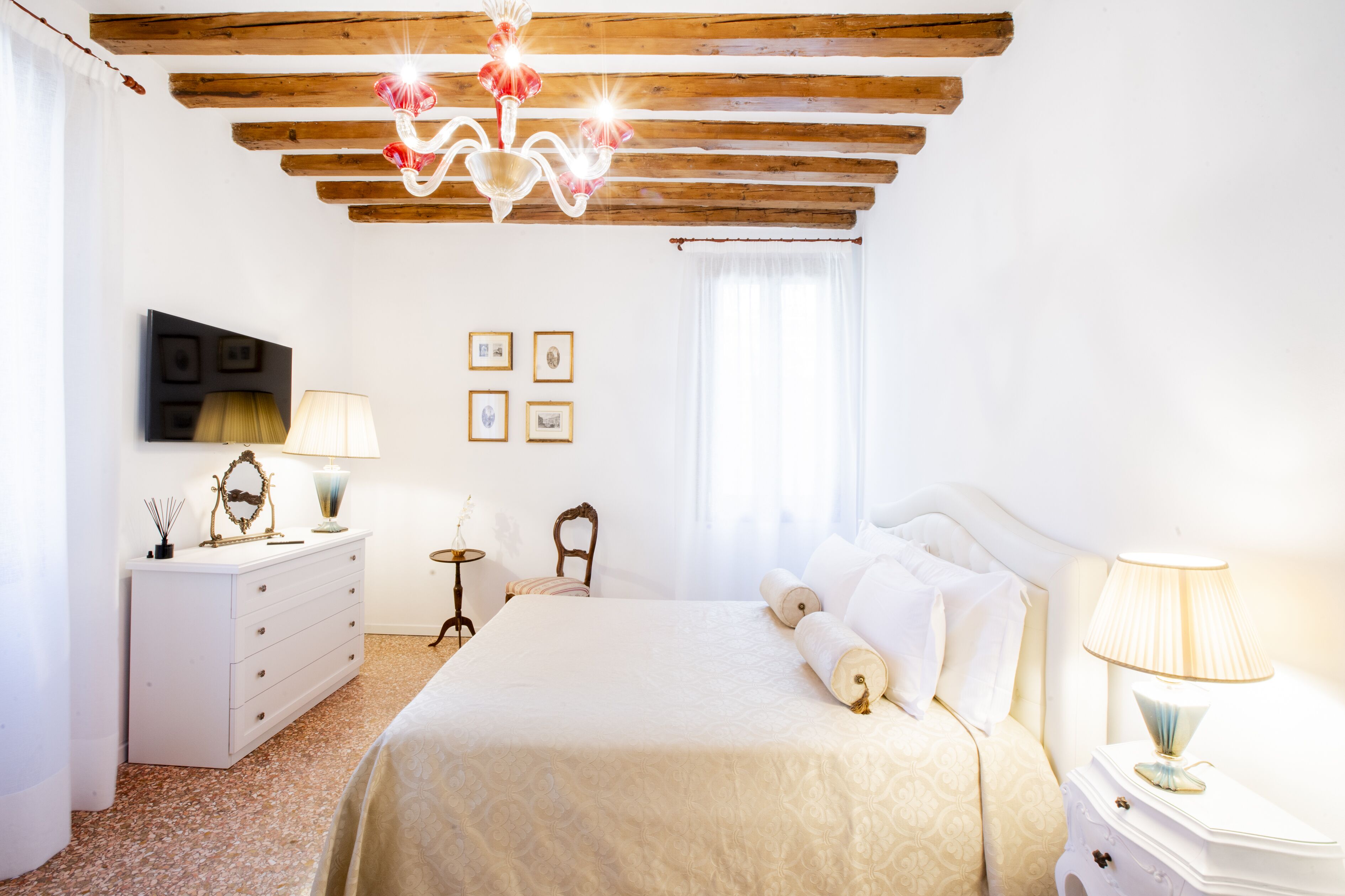 A bedroom with a bed, a dresser, a nightstand, a lamp, a mirror, and a chandelier.