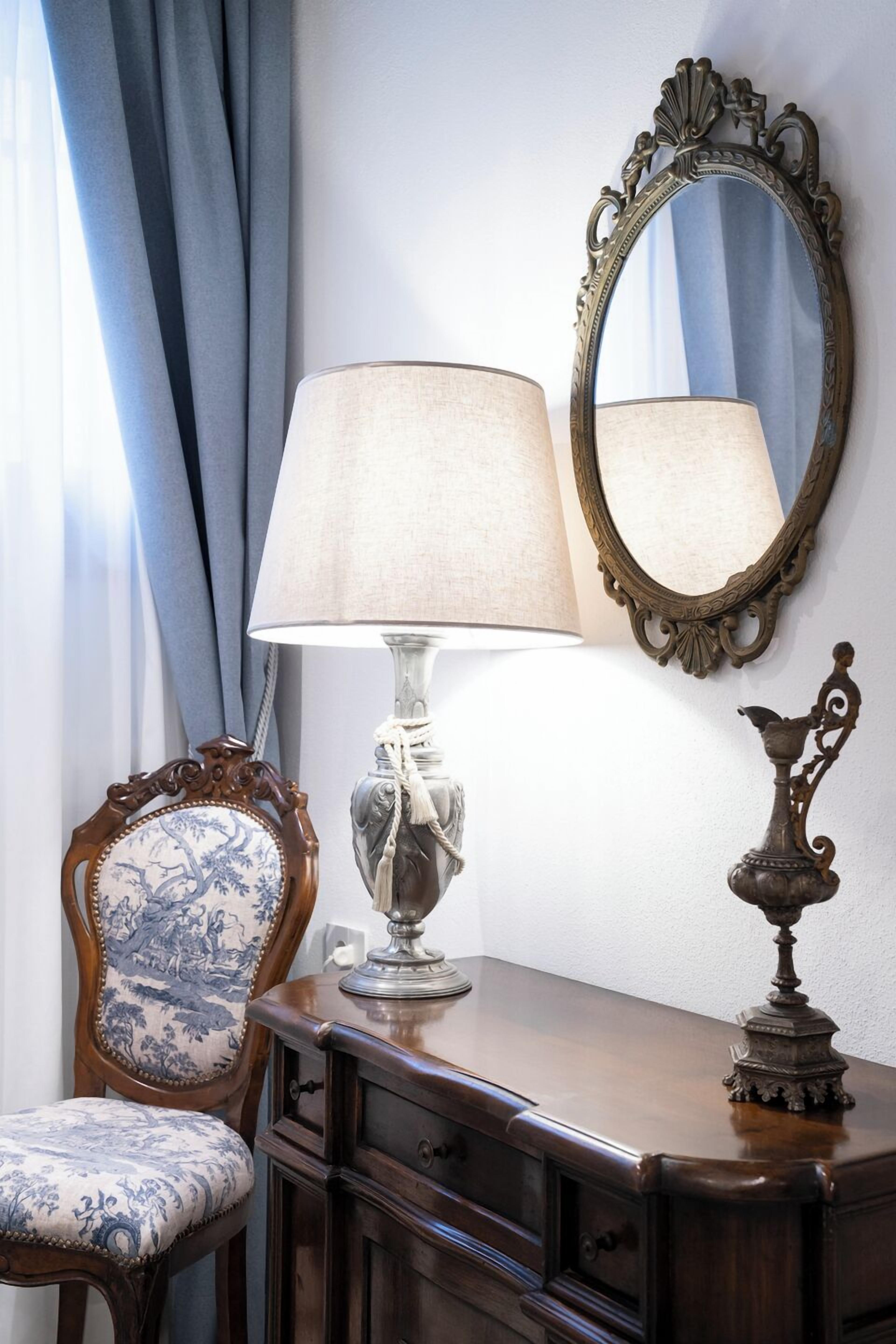A wooden dresser with a lamp, a mirror, and a decorative vase.
