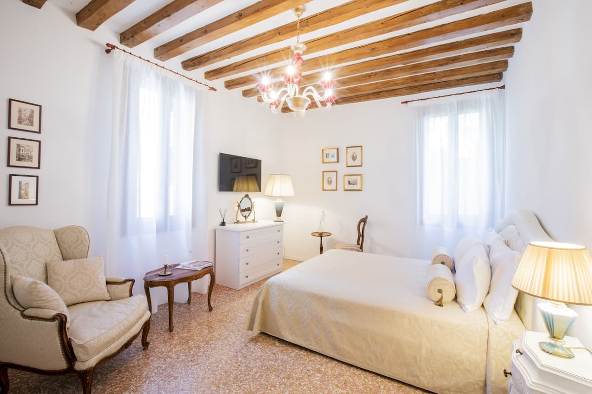 A bedroom with a bed, a chair, a dresser, a lamp, and a television on the wall.
