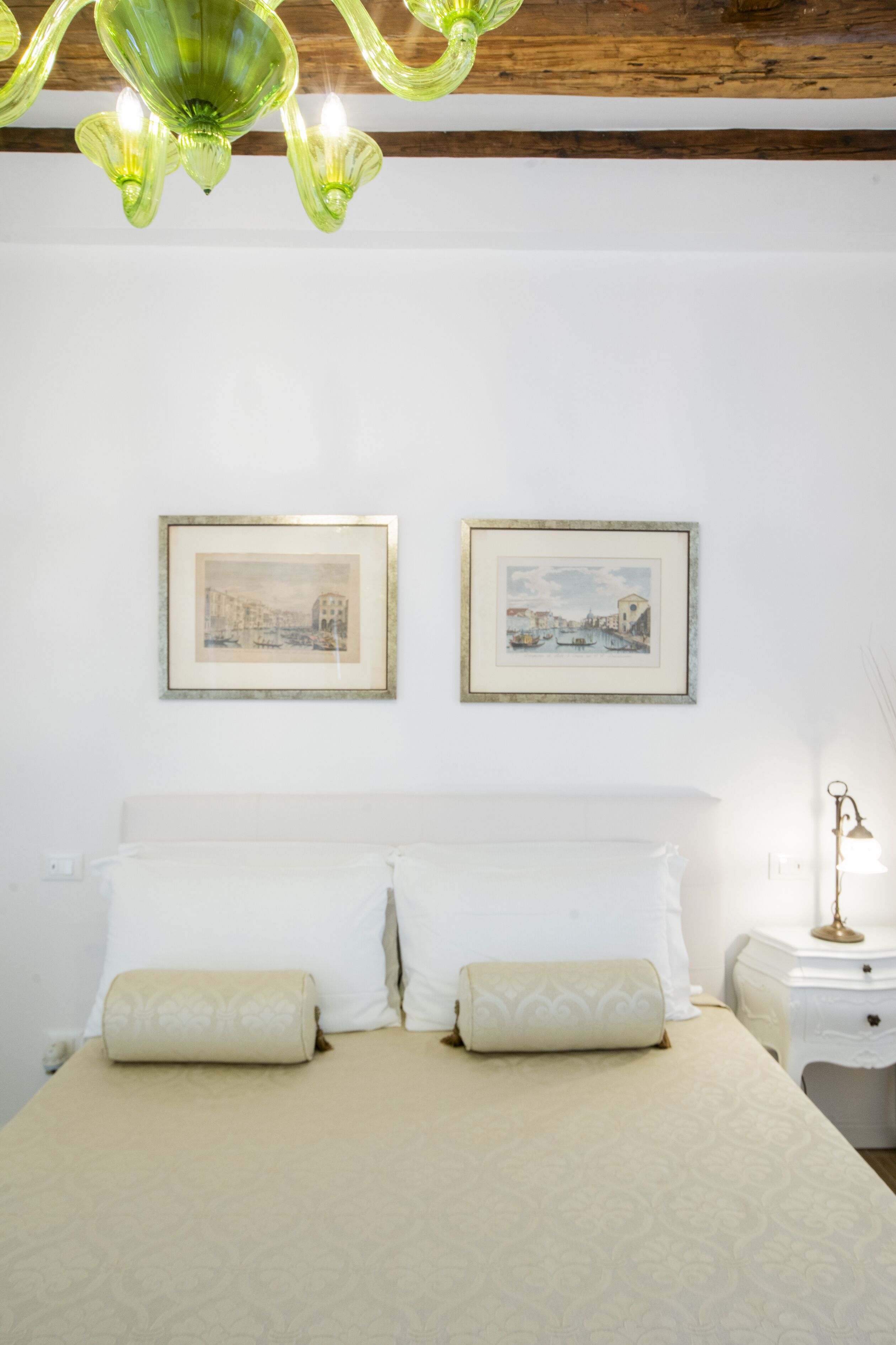 Ein ordentlich eingerichtetes Schlafzimmer mit einem Bett, zwei gerahmten Bildern an der Wand, einer Nachttischlampe und einem grünen Chandelier.