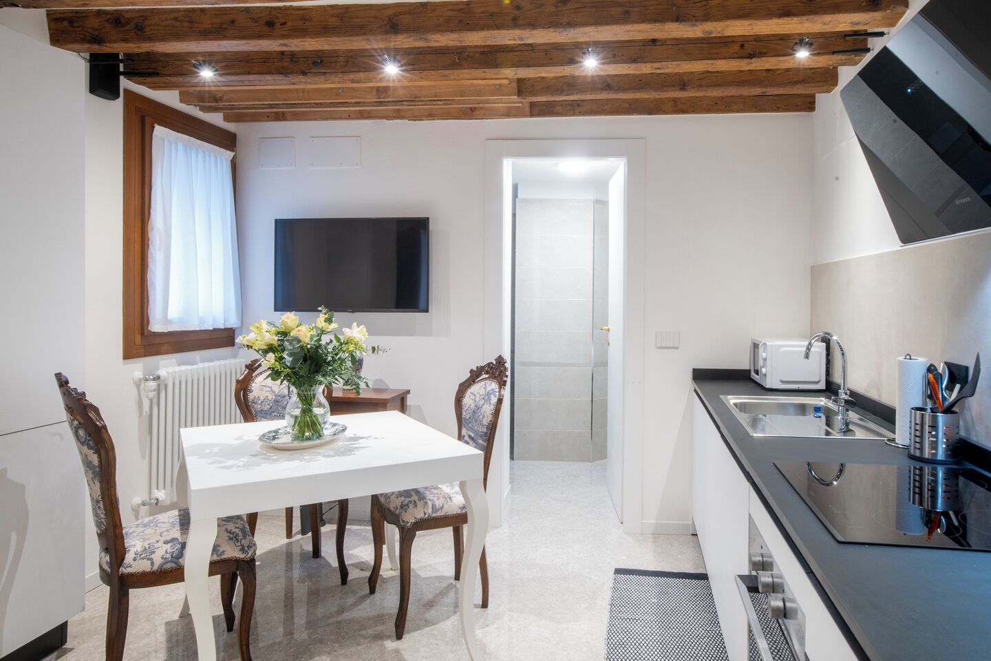 Cocina moderna con comedor, que incluye una mesa blanca, sillas de madera, un televisor y un microondas.