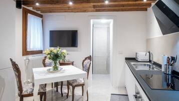 Cocina moderna con comedor, que incluye una mesa blanca, sillas de madera, un televisor y un microondas.