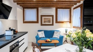 A living room with a blue sofa, a wooden table, and a vase of flowers. There is a kitchen area with a stove and a toaster. - Giò&Giò Apartments (Venice)