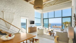 A spacious living area with a large window overlooking the sea, a wooden dining table, and a modern interior design. - Villa Anton by Cura Villas Collection (Chania)