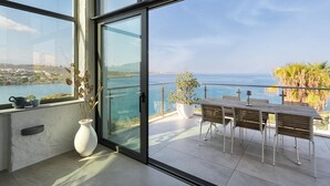 A balcony with a table and chairs, a potted plant, and a view of the sea. - Villa Anton by Cura Villas Collection (Chania)