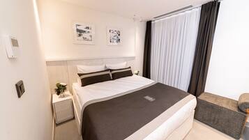 A modern hotel room with a large bed, a bedside table with a lamp, and a window with curtains.