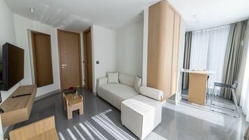A modern hotel room with a sofa, a small table with a vase, a TV, and a desk with a chair.