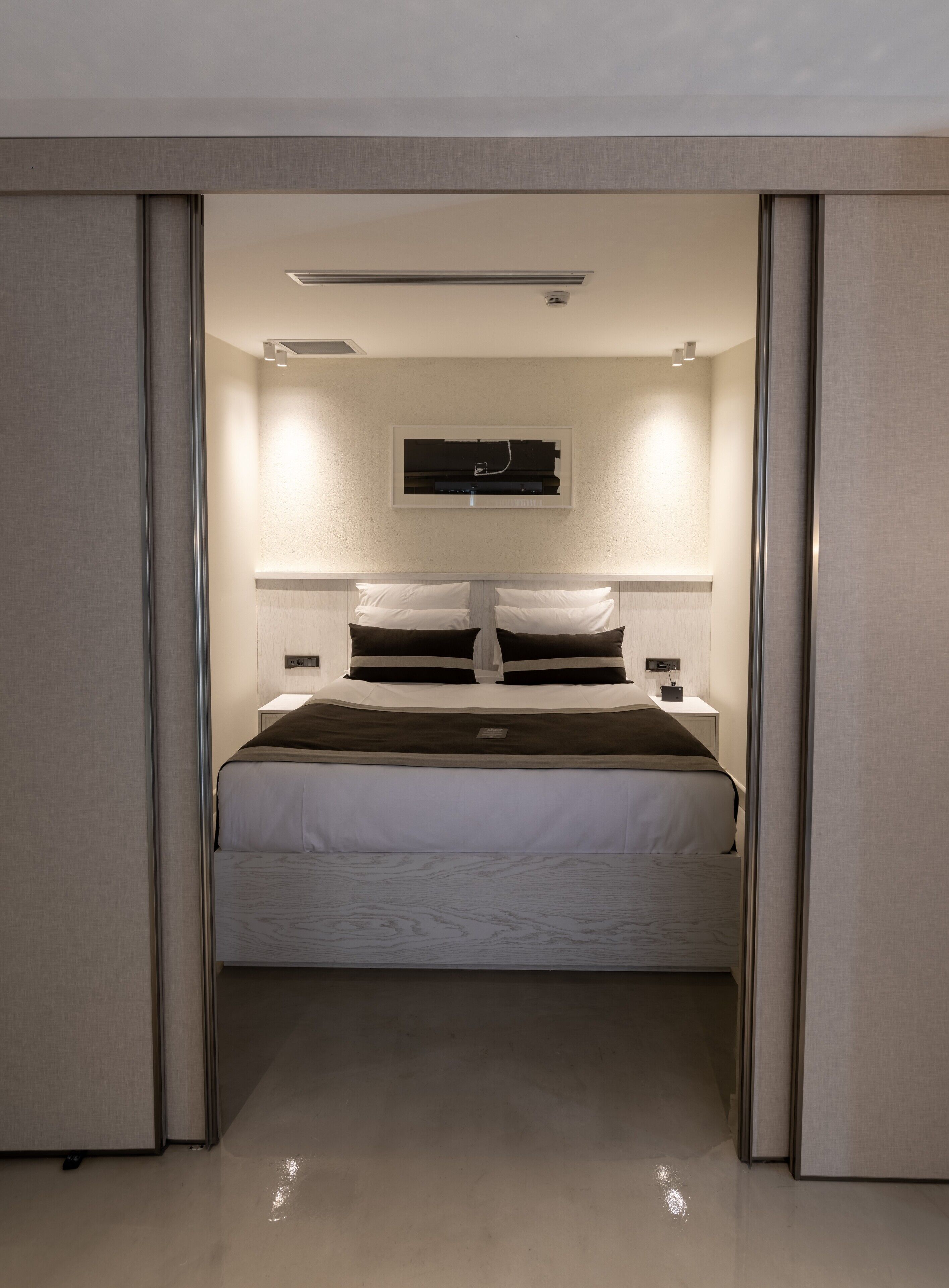 Un dormitorio moderno con una cama centrada bajo una lámpara del techo, flanqueada por dos mesitas de noche con lámparas.