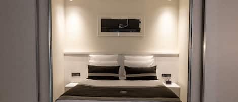 Un dormitorio moderno con una cama centrada bajo una lámpara del techo, flanqueada por dos mesitas de noche con lámparas.