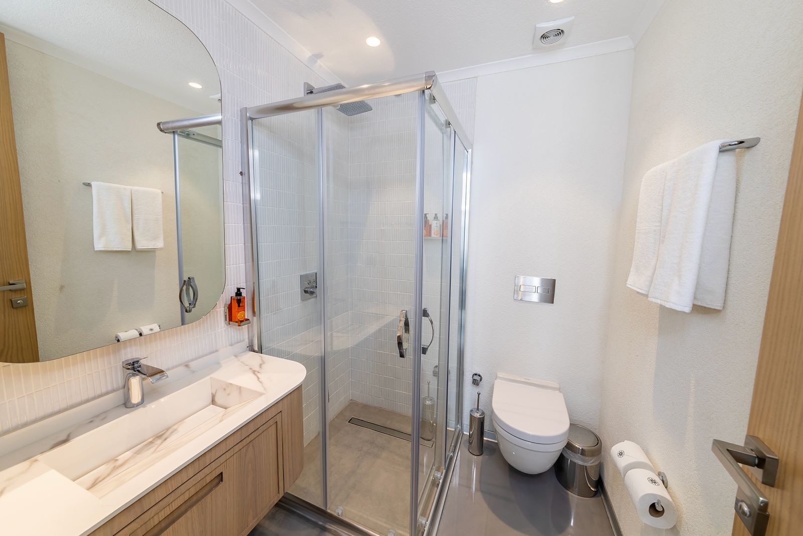 A modern bathroom with a glass shower enclosure, a white toilet, and a vanity with a mirror.
