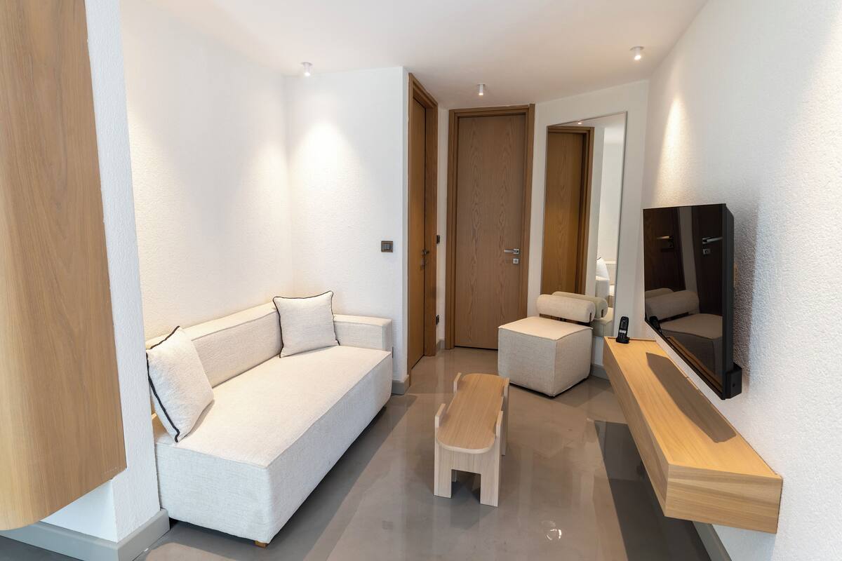 Quarto de hotel moderno com sofá, uma mesinha e uma TV fixada na parede.