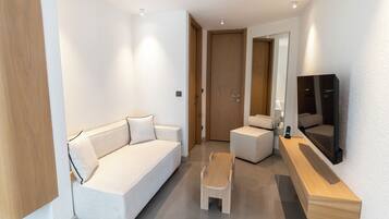 A modern hotel room with a sofa, a small table, and a TV mounted on the wall.