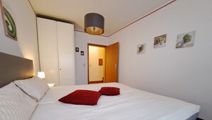 A hotel room with a bed, a wardrobe, a door, and wall-mounted pictures.