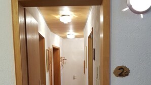 A hallway with wooden doors, a carpeted floor, and a light fixture on the wall.