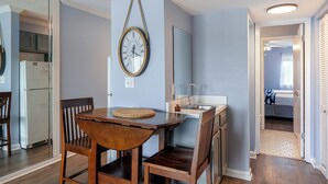 A dining area with a wooden table and chairs, a wall-mounted clock, and a kitchen with a refrigerator and cabinets. - Fall Dates Available! Quick Walk to Beach! Perfect for Families! (Panama City Beach)