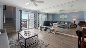 A modern living room with a flat-screen TV, a ceiling fan, and a glass partition. - Fall Dates Available! Quick Walk to Beach! Perfect for Families! (Panama City Beach)