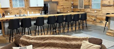 A cozy cabin interior with a wooden wall adorned with deer heads, a kitchen area, and a seating arrangement.