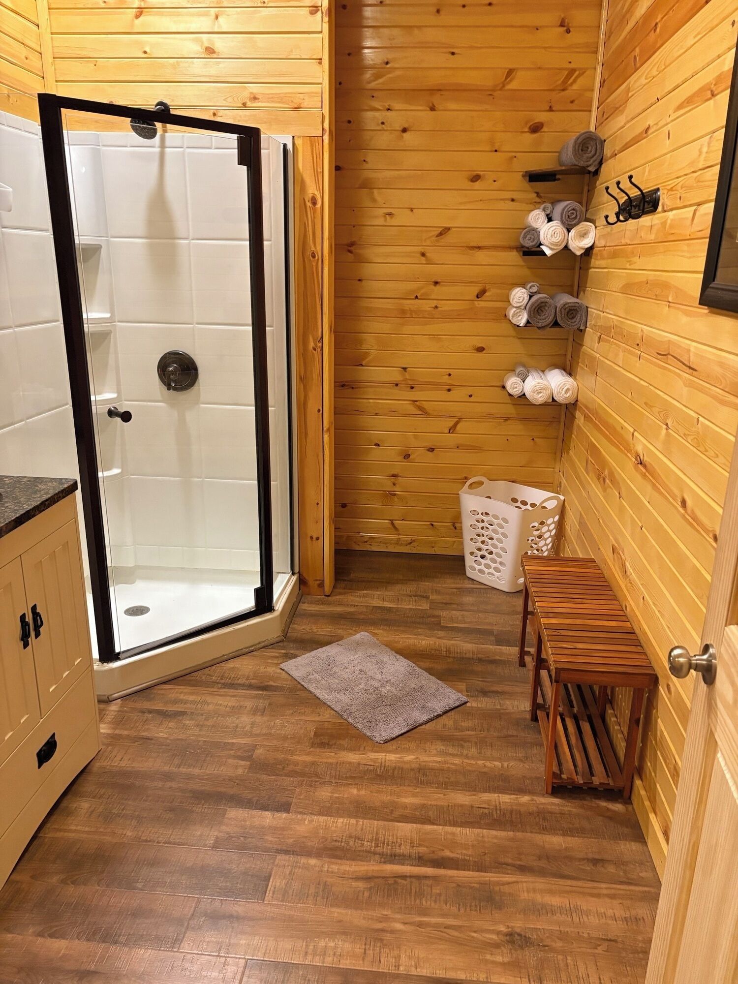 Un intérieur en bois avec une cabine de douche en verre, un banc en bois et un panier à linge.