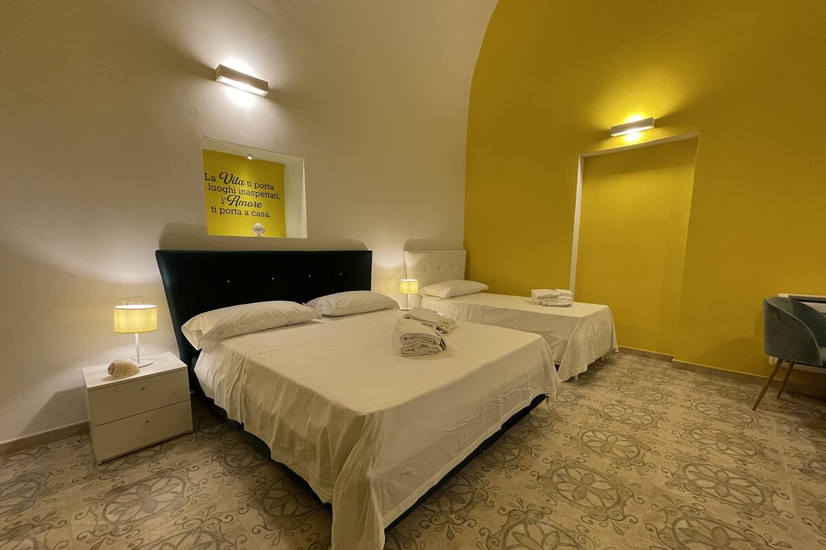 A hotel room with two beds, a nightstand, a lamp, and a wall-mounted sign.