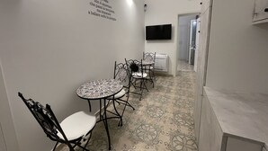 A narrow hallway with a dining area featuring a mosaic table and metal chairs. A wall-mounted TV and a thermostat are visible. - Donna Grazia  (Gallipoli)