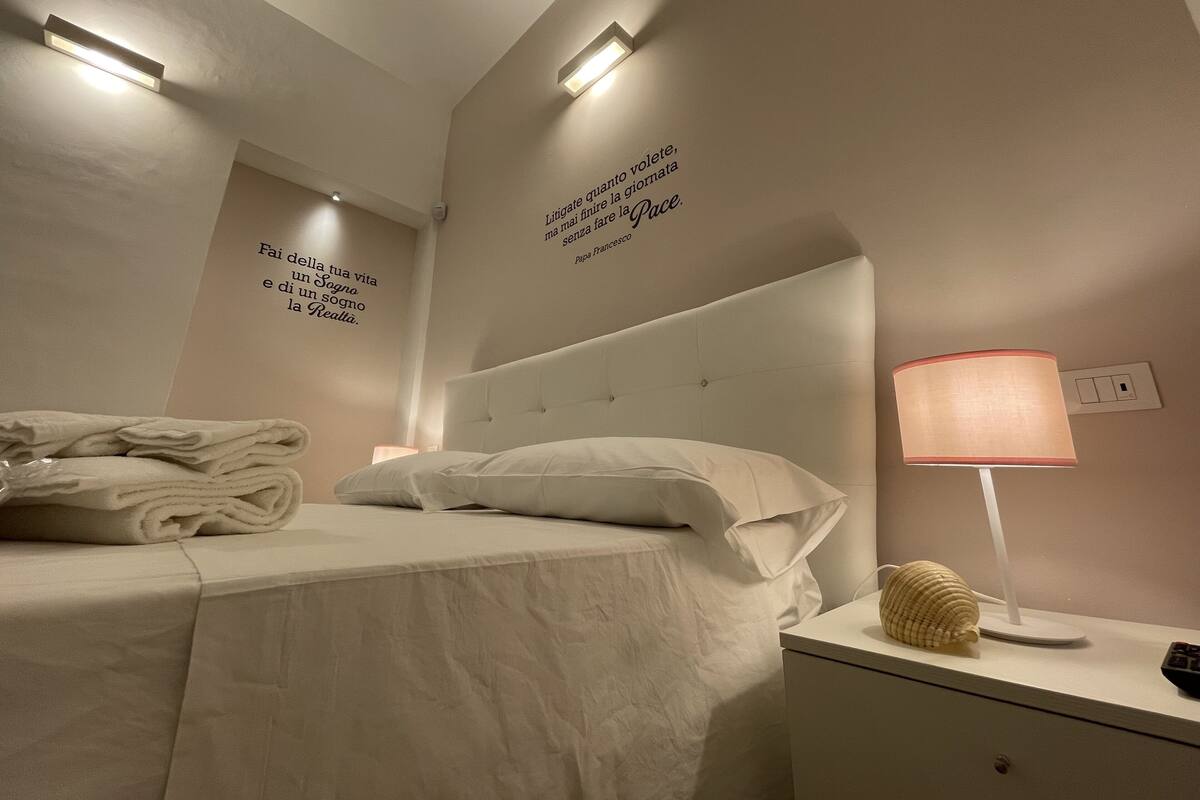 A neatly made bed with pillows and a folded towel, a bedside lamp, and a decorative shell on the nightstand.