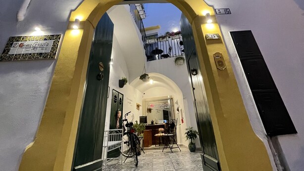 A building entrance with an arched doorway, a balcony with plants, and a sign with a name. - Donna Grazia  (Gallipoli)
