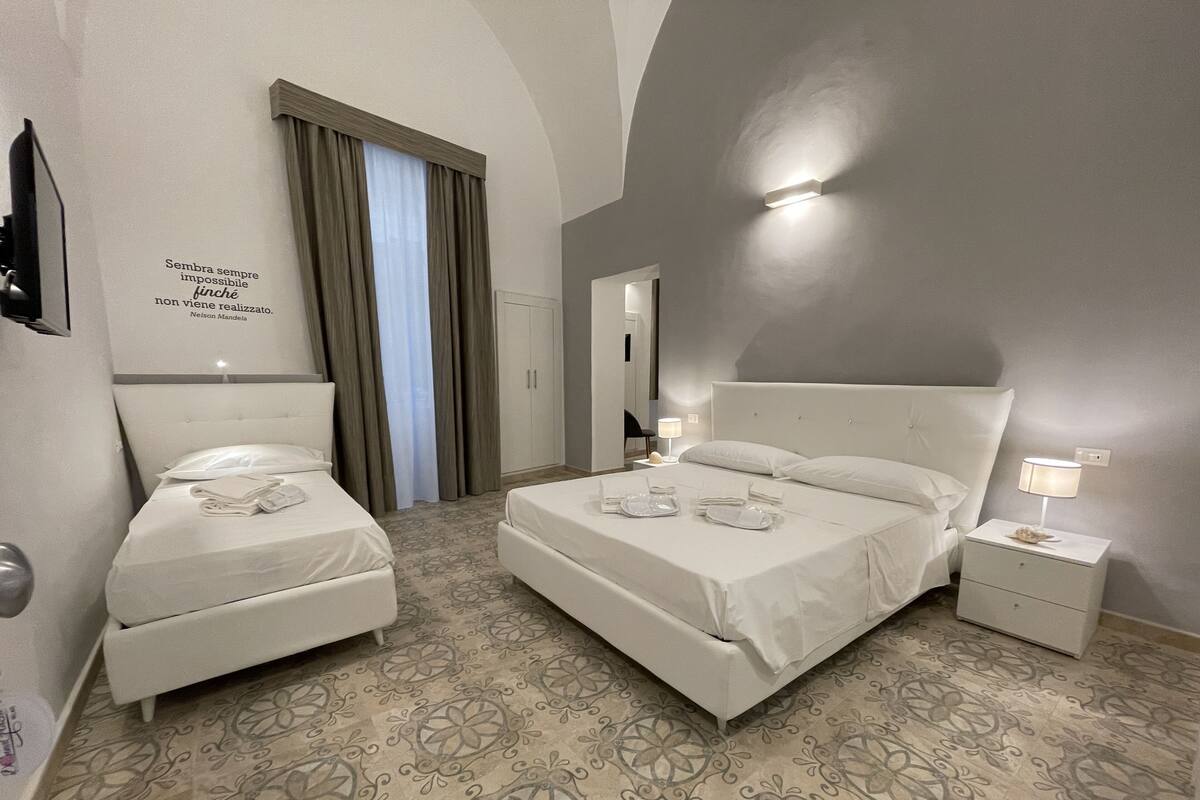 A hotel room with two beds, a wardrobe, a mirror, and a decorative quote on the wall.