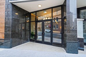 A building entrance with a glass door marked "505," a paved entrance area, and a reflection of a street scene. - La Luz (San Antonio)
