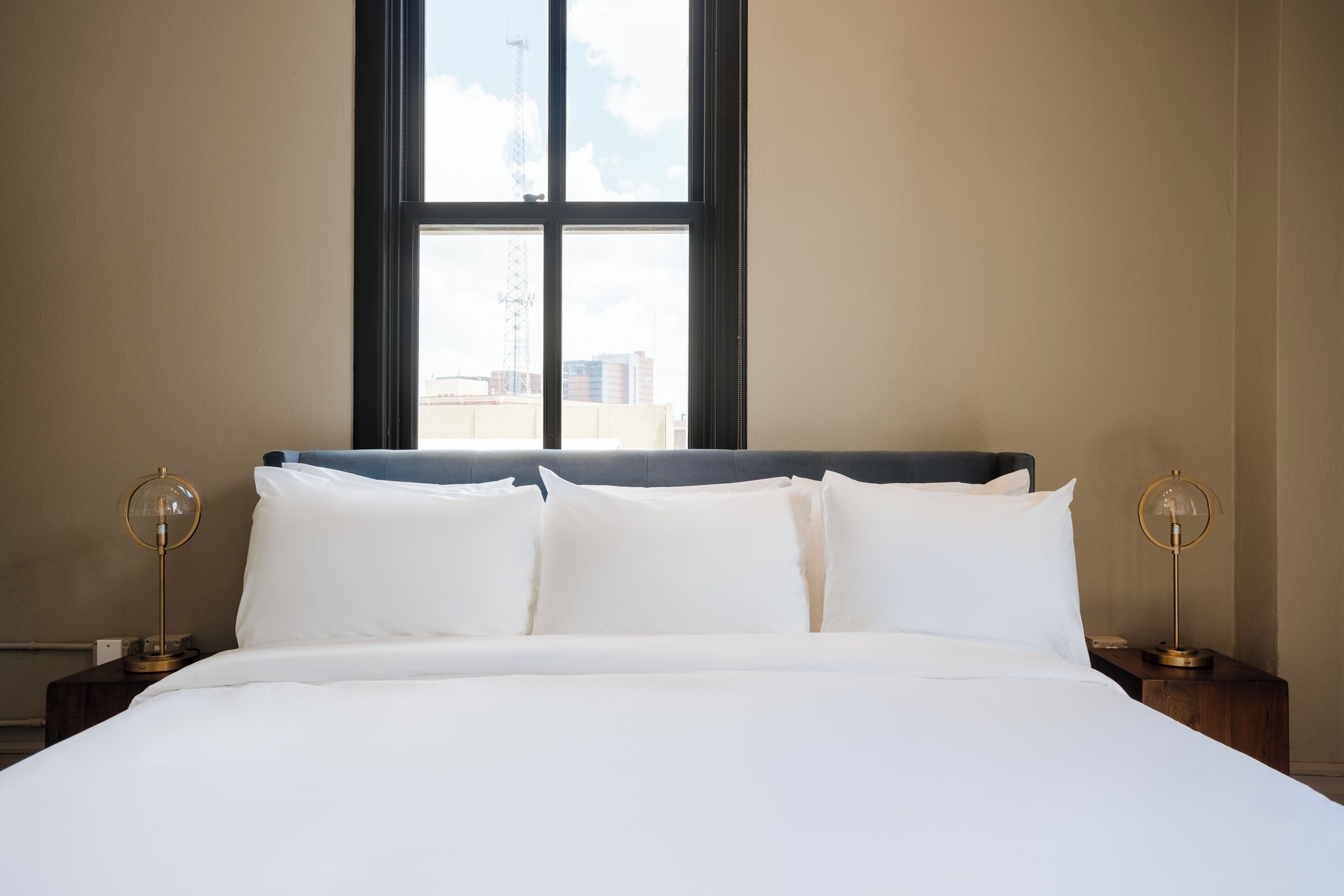 A neatly made bed with white linens, a dark headboard, and two bedside lamps with round bases.