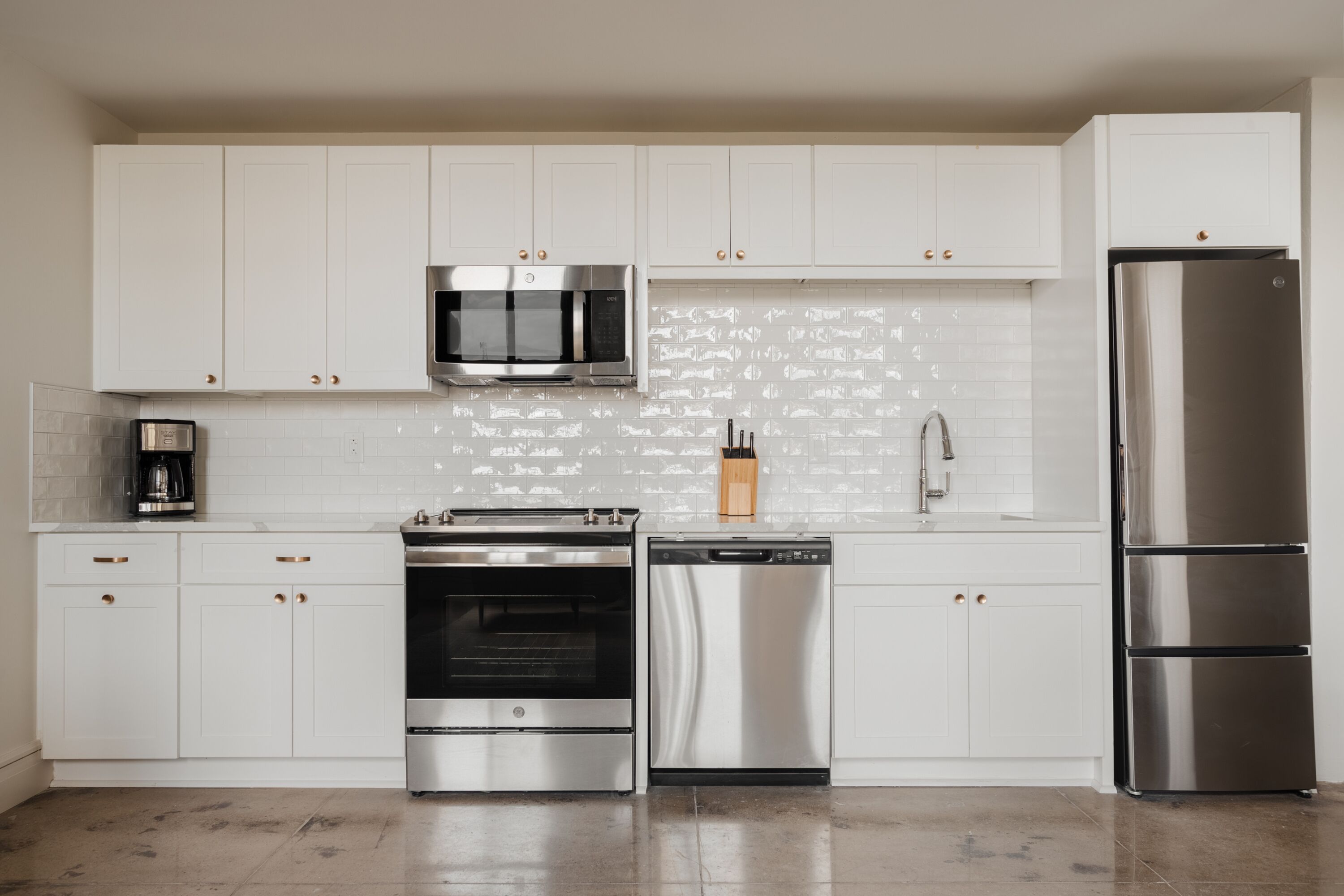 A modern kitchen with white cabinets, stainless steel appliances, and a tiled backsplash.