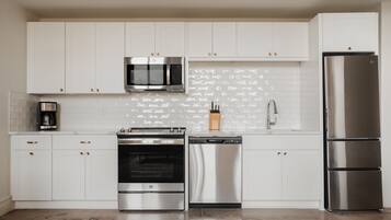 A modern kitchen with white cabinets, stainless steel appliances, and a tiled backsplash.