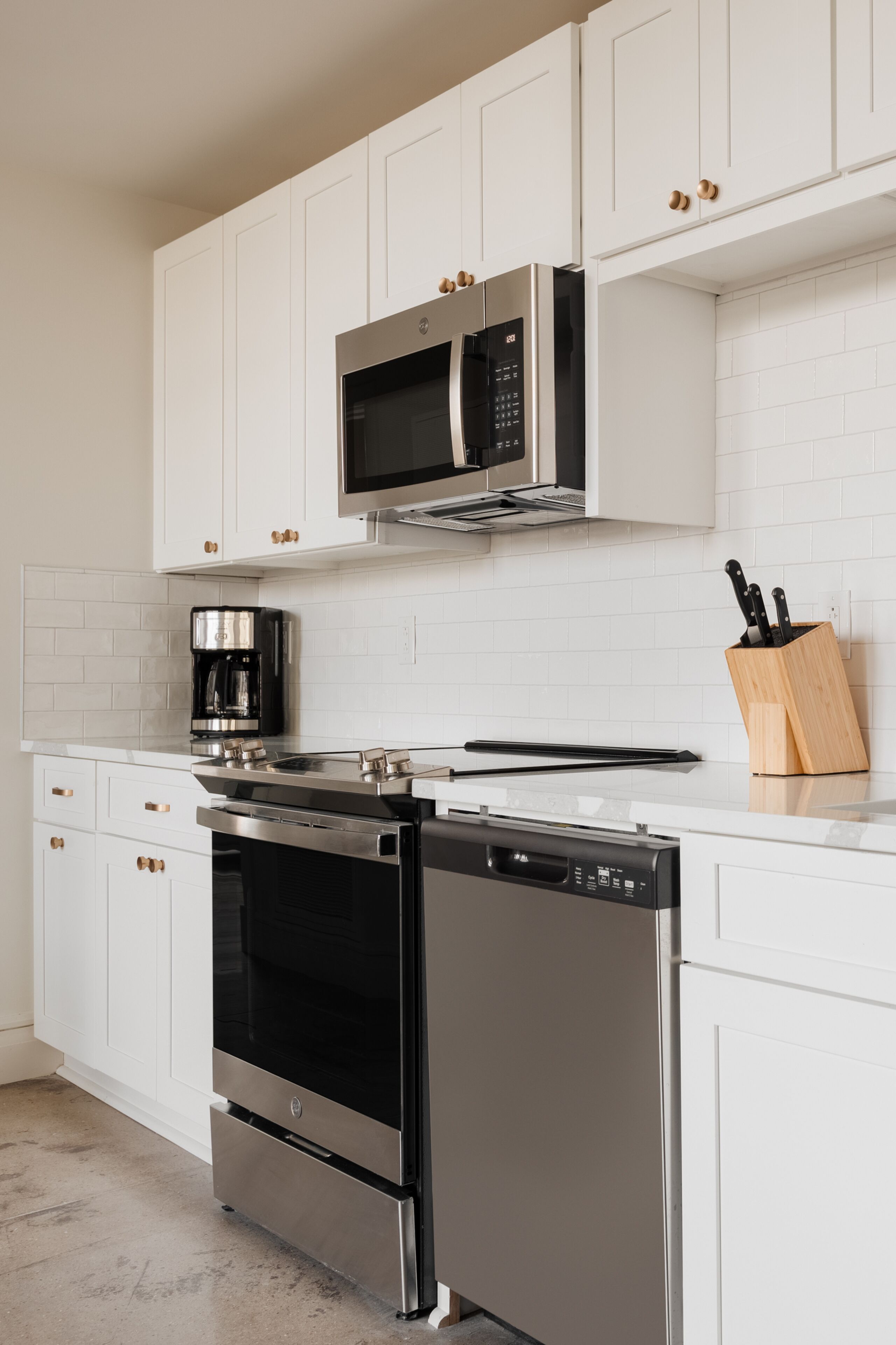 A modern kitchen with white cabinetry, stainless steel appliances, and a coffee maker.