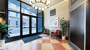 Recepció d'hotel amb terra de pissos, dos seients còmodes, una taula petita, una planta en test i un gran finestral amb vista al carrer.