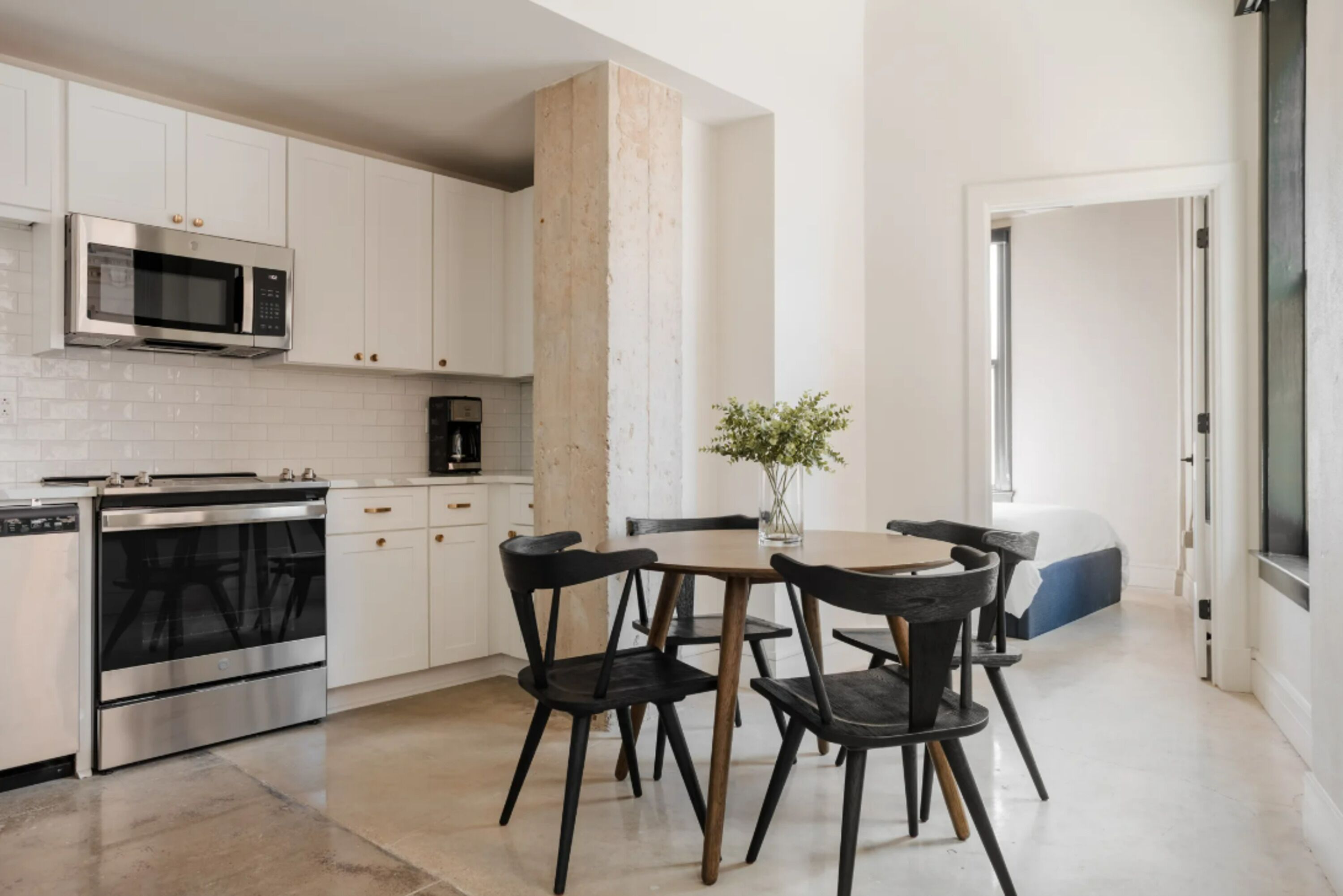 A modern kitchen with white cabinets, a built-in microwave, a stove, and a dining area with a table and chairs.