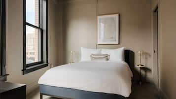 A modern bedroom with a large bed, a window, a framed artwork, and two bedside lamps.