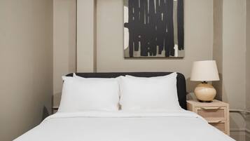 Una cama bien hecha con sábanas blancas, una lámpara de noche y una obra de arte abstracta en la pared.