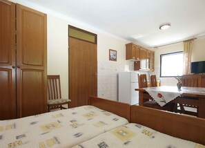 Une pièce de taille modeste comprenant un lit, une table à manger avec des chaises, un réfrigérateur, des placards en bois et une fenêtre avec des rideaux.
