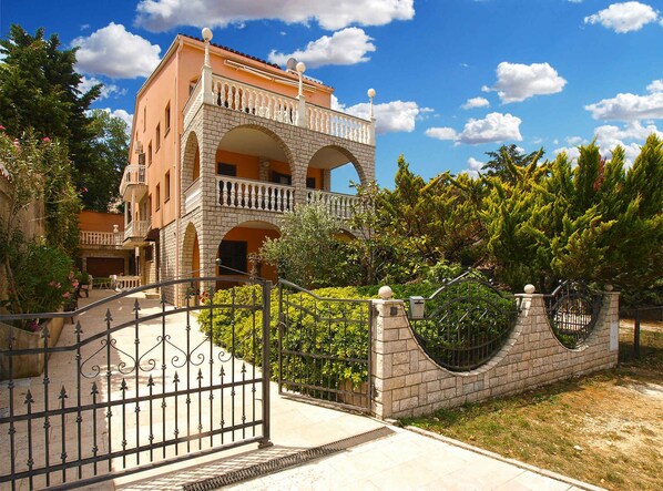 A multi-story building with a balcony, a gated entrance, and surrounding greenery.