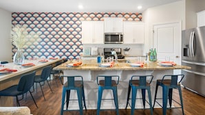 A modern kitchen with white cabinets, a stainless steel refrigerator, and a patterned backsplash. - 6min to UNCC: Spacious 5bd with Games Backyard (Charlotte)