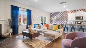 A modern living room with a sofa, coffee table, and bar stools. There is a kitchen area with a microwave and bar counter. - 6min to UNCC: Spacious 5bd with Games Backyard (Charlotte)