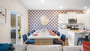 A dining area with a table set for six, surrounded by blue chairs, and a kitchen with white cabinets and a microwave. - 6min to UNCC: Spacious 5bd with Games Backyard (Charlotte)