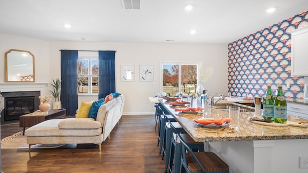 A modern living room with a fireplace, a sofa, and a dining area with a kitchen island. - 6min to UNCC: Spacious 5bd with Games Backyard (Charlotte)