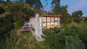 A modern two-story house with a large glass facade, situated on a hillside with surrounding trees. - Summitridge - An Elegant Estate with Unobstructed City and Ocean Views (Beverly Hills)