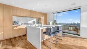 A modern kitchen with wooden cabinets, a marble countertop, and a large window offering a view of the city. - Summitridge - An Elegant Estate with Unobstructed City and Ocean Views (Beverly Hills)