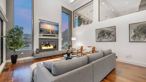 A modern living room with a fireplace, a large sofa, and artwork on the walls. - Summitridge - An Elegant Estate with Unobstructed City and Ocean Views (Beverly Hills)