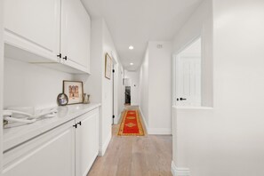 Stunning hallway with a red and gold patterned rug leading to a door, featuring a white countertop with a framed picture and a clock.
